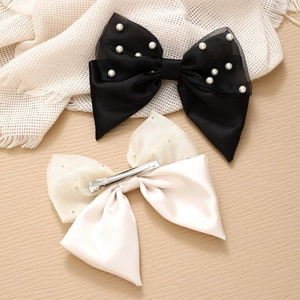 Detail of elegant satin bow hair clips with pearls and rhinestones on textured fabric