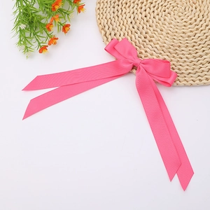 Close-up of rose pink ribbed ribbon bow hair clip with long streamers on white background
