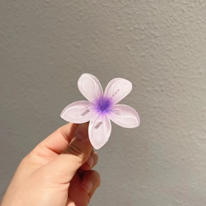 Détail d'une pince à cheveux fleur dégradé violette tenue à la main pour l'échelle