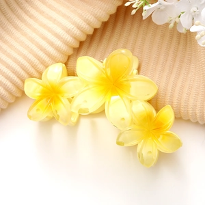 Détail d'une pince à cheveux fleur de frangipanier jaune sur un tissu en maille beige