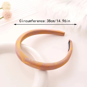 Elegant gold paisley satin headband with purple floral embroidery on a white ceramic tray