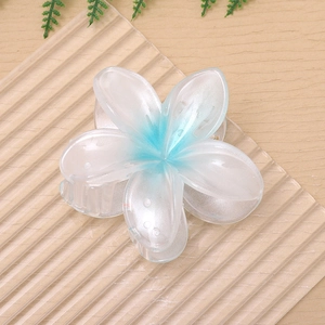 Detail view of a large blue and white plumeria flower claw clip on a light wooden table