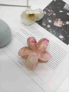 Detail of pink marble textured resin plumeria claw clip with golden metal spring
