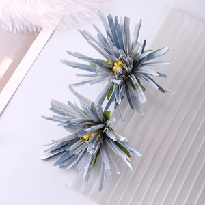 Detail view of two blue fabric chrysanthemum hair clips on a minimalist white background