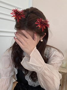 Macro detail of red spider lily hair clips worn on the side of a model's hair
