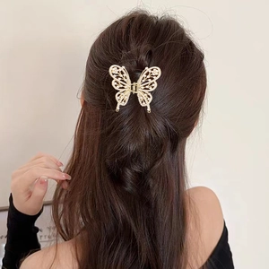Détail d'une pince à cheveux papillon dorée avec perles sur des cheveux bouclés