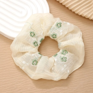 Close-up of beige chiffon scrunchie with delicate green floral embroidery on wood surface