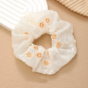Detailed close-up of a floral chiffon scrunchie with orange flower embroidery on wood