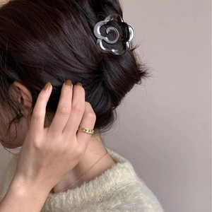 Détail d'une pince à cheveux camélia gris foncé translucide sur un chignon élégant de femme
