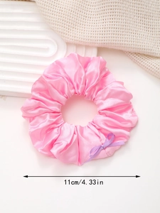Gros plan sur chouchou en satin rose avec nœud et mesure de diamètre de 11 cm