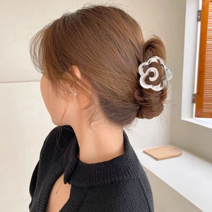 Pince à cheveux fleur rose en métal argenté portée sur un chignon pour femme