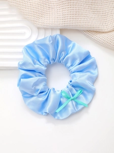 Détail d'un chouchou en satin bleu clair avec un nœud vert pastel sur un plateau