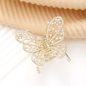 Détail d'une pince à cheveux papillon dorée avec perles et ailes métalliques ajourées