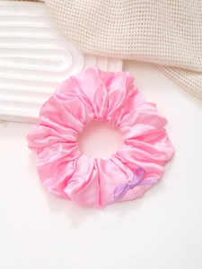 Gros plan sur un chouchou en satin rose avec un nœud lilas sur fond blanc élégant