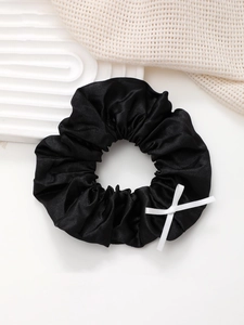 Gros plan d'un chouchou en satin noir avec nœud blanc sur un plateau blanc texturé