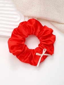 Détail d'un chouchou en satin rouge brillant orné d'un délicat nœud en ruban de couleur crème