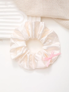 Détail d'un chouchou en satin champagne avec un nœud rose sur un plateau texturé