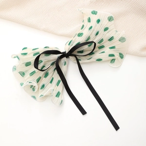 Detail view of large white bow hair clip with green polka dots and black ribbon accent