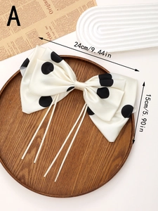 Close-up of a large white silk bow hair clip with black polka dots on a wooden tray