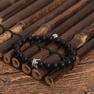 Detailed macro view of black matte beaded bracelet featuring a vintage silver crown charm