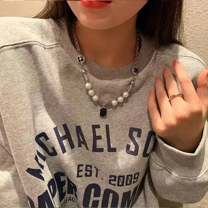 Detailed view of pearl necklace with black rectangle pendant on a gray sweatshirt