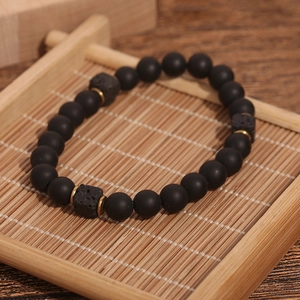 Men's matte black agate beaded bracelet with lava stone cubes and gold accents on bamboo