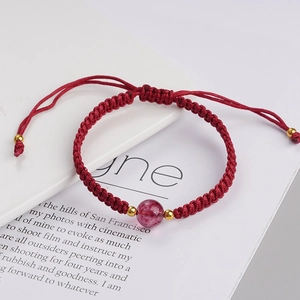 Detail eines roten geflochtenen Armbands mit rosa Kristallperle und Goldakzenten