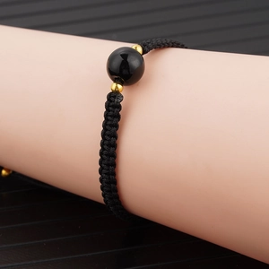 Detail eines handgewebten schwarzen Armbands mit Obsidian-Perle und Goldakzenten