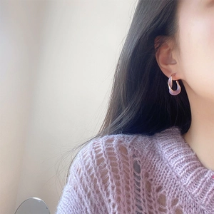 Détail de créoles dorées avec émail violet clair portées sur l'oreille