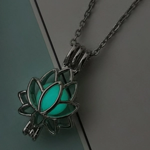 Gros plan du pendentif lotus ajouré avec une perle verte lumineuse dans l'obscurité