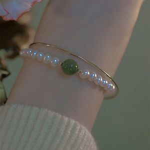 Detailopname van een gouden armband gecombineerd met een parelarmband met groene kraal