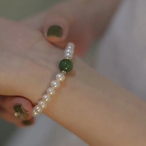 Detailopname van een parelarmband met donkergroene jade kraal en gouden accenten