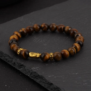 Macro shot of tiger eye beads with golden buddha head charm on dark stone background