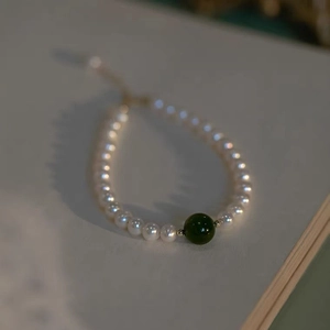 Detail van een parelarmband met een donkergroene jade kraal en gouden accenten erop