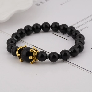 Detail of luxury men's bracelet with black beads and two golden crown alloy charms