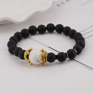 Detailed close-up of luxury crown charms and white marble beads on a black beaded bracelet