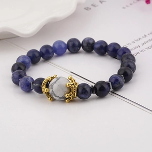 Detailed macro view of natural blue stone beads bracelet with a golden crown charm and white bead