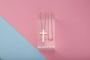 Gepolijste roségouden kruishanger aan ketting op acrylstandaard met pastelkleuren