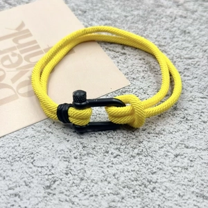 Détail d'un bracelet en corde de nylon tressé jaune avec manille en métal noir mat en forme de U
