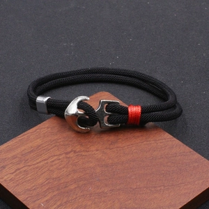 Détail d'un bracelet nautique en corde noire avec fermoir ancre argenté sur support bois