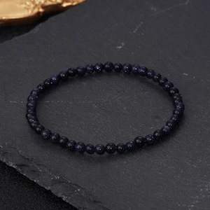 Macro shot of 4mm blue goldstone energy bead bracelet on a textured rock background