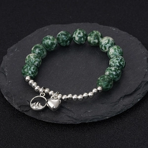 Bracelet de perles en pierre verte avec breloques cœur et montagne sur un rocher sombre