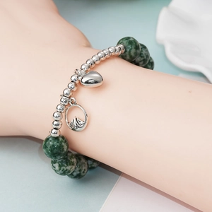 Détail du bracelet avec perles en pierre verte et breloques cœur et montagne en argent