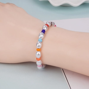 Hand wearing a colorful pearl beaded bracelet with mixed vibrant beads on blue background