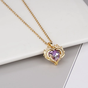 Macro detail of gold necklace with a purple heart pendant and white diamond accents