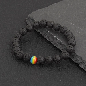 Black lava rock beaded bracelet with a rainbow accent bead on a dark stone background