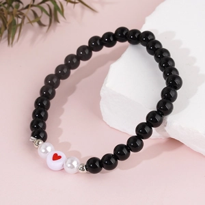Bracelet en obsidienne noire et perles avec cœur exposé sur une pierre décorative blanche