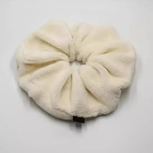 Close-up of oversized plush cream scrunchie with soft faux fur texture and black woven label