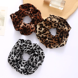 Three leopard print scrunchies in brown, tan, and black with pleated velvet texture