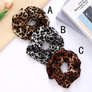 Three leopard print scrunchies with pleated texture on a decorative beige fabric background